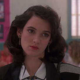 winona ryder, a white feminine person with brown hair and eyes is staring at something off camera with a neutral face.